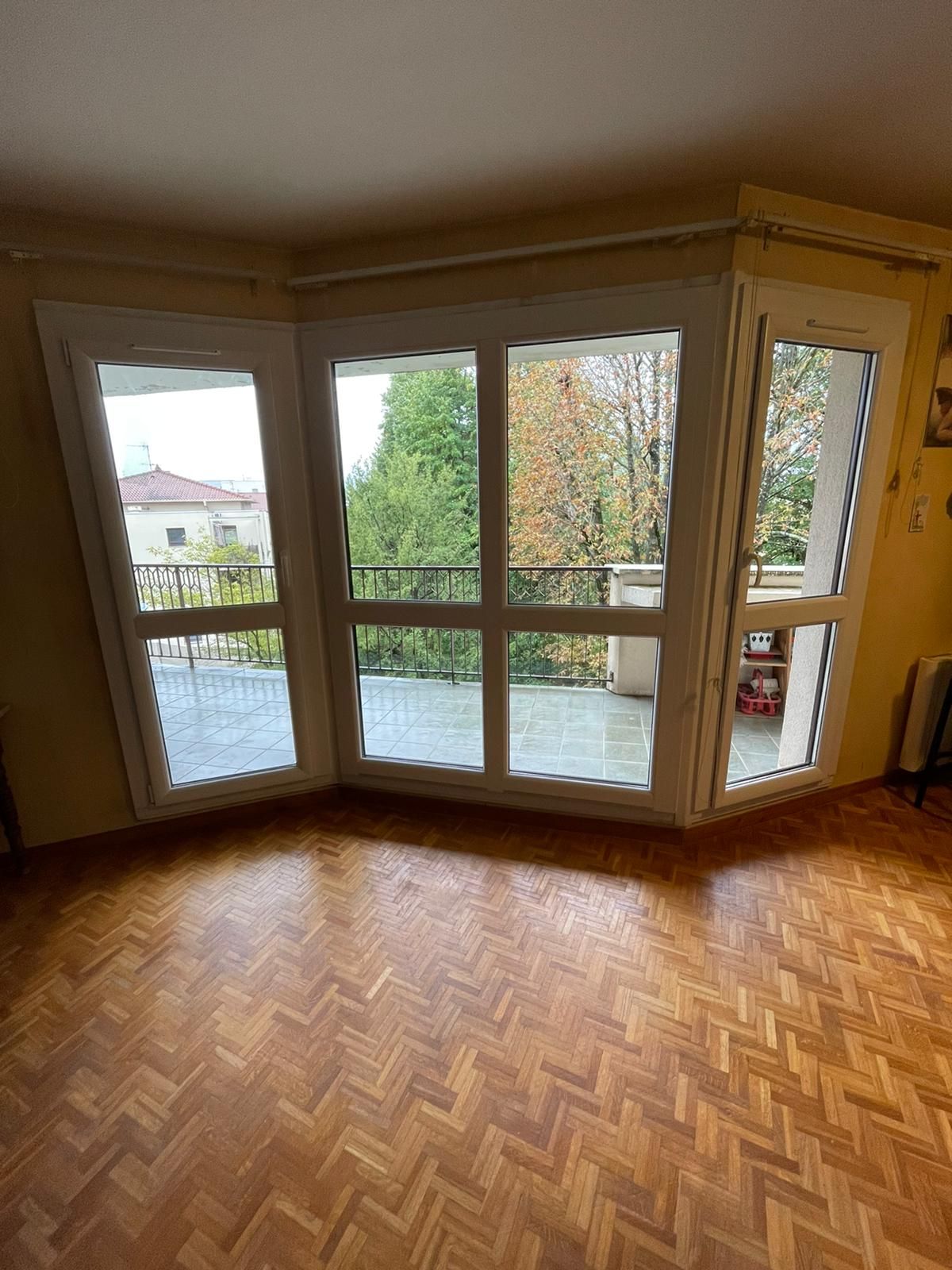 Ensemble de fenêtres blanches en angle et porte-fenêtre ouvrant sur une terrasse, dans une pièce au parquet