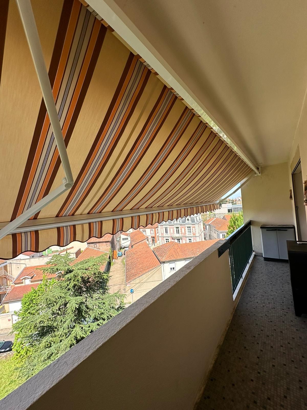 Store banne à rayures déployé au-dessus d'un balcon, avec vue sur les toits de la ville